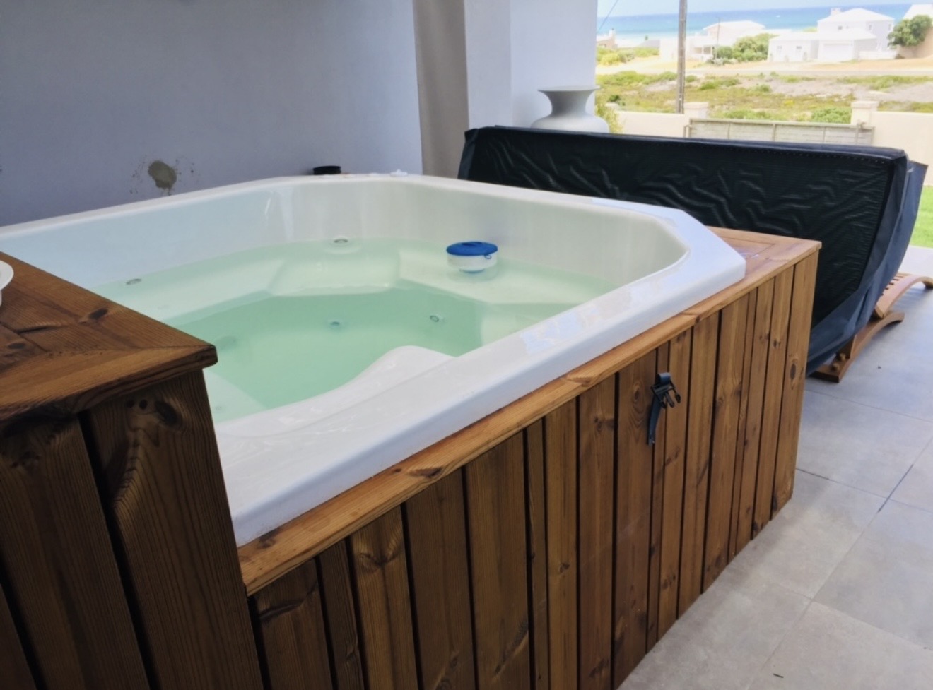 Jacuzzi with timber cladding installed on a covered patio with a sea view