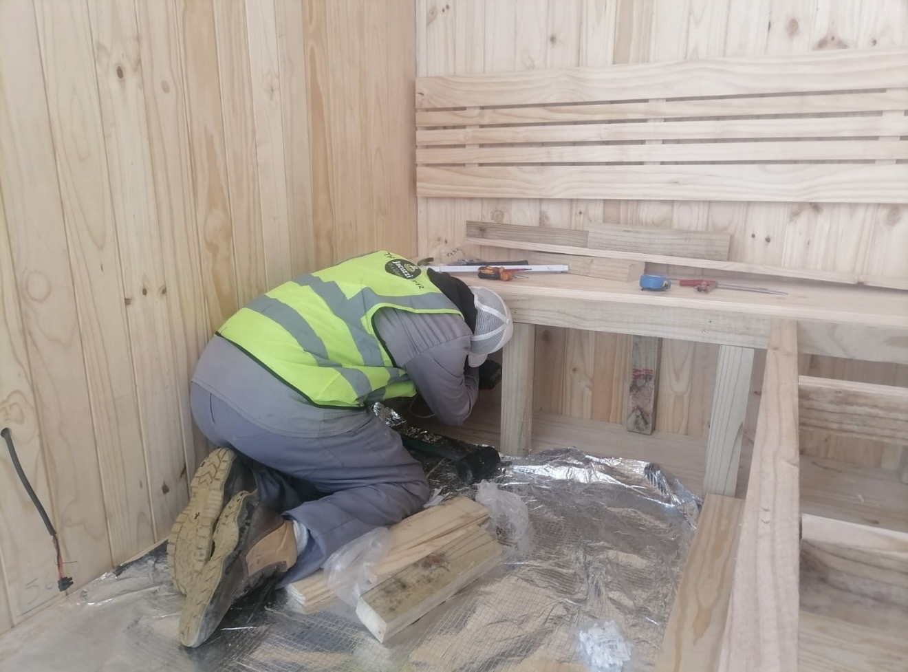 Technician fitting a pine bench inside a sauna under construction