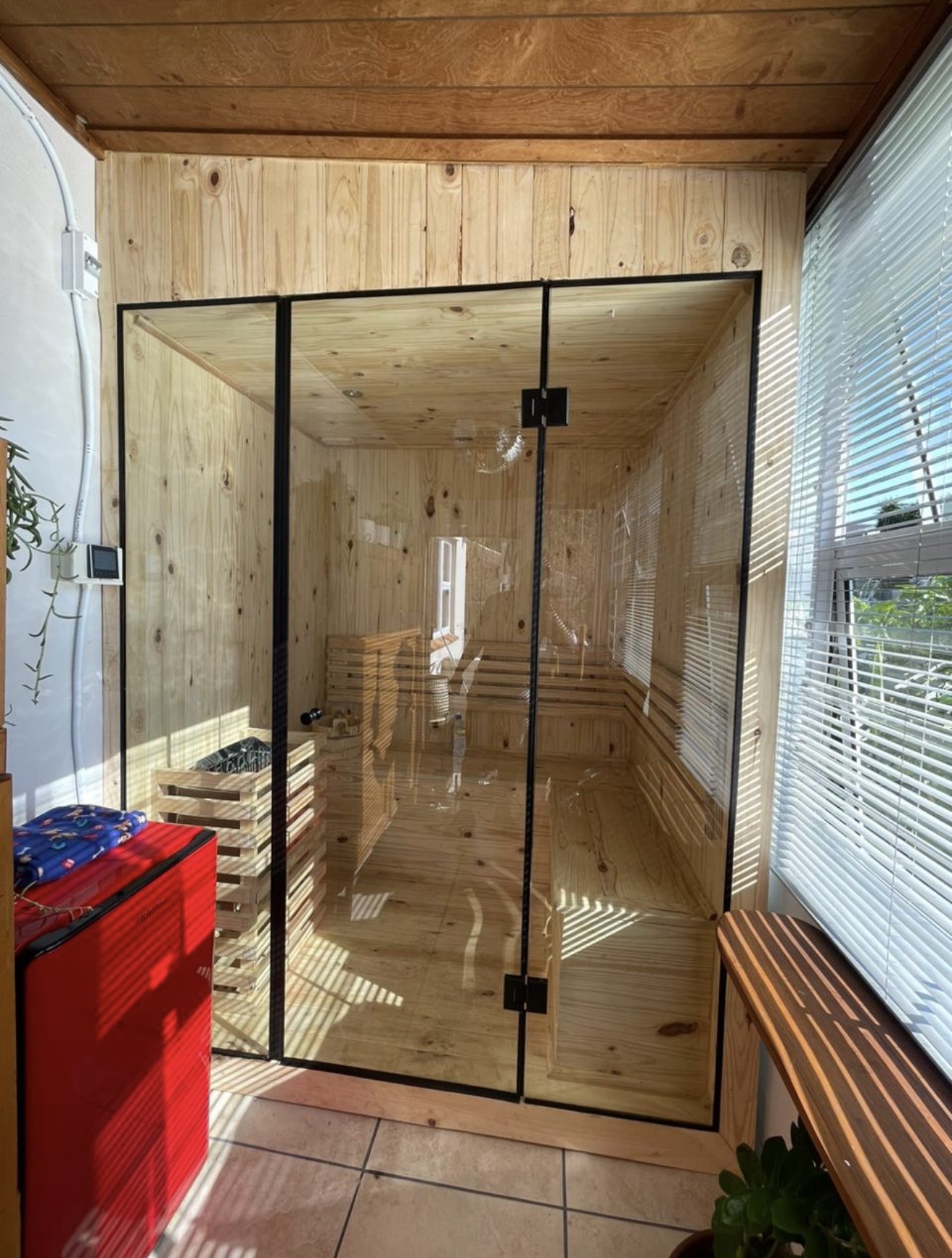 Glass-front sauna cabin fitted in a sunroom with an external digital control panel