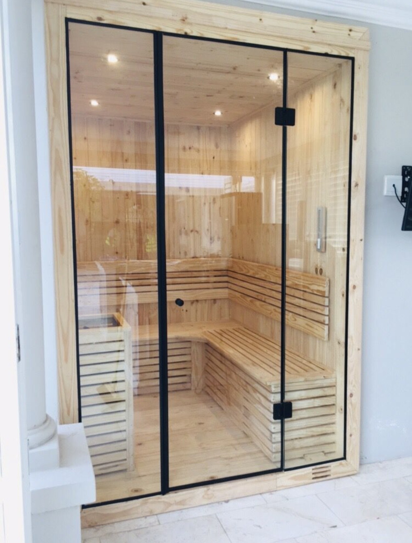 Finished indoor sauna with an L-shaped slatted bench and a full-height glass front