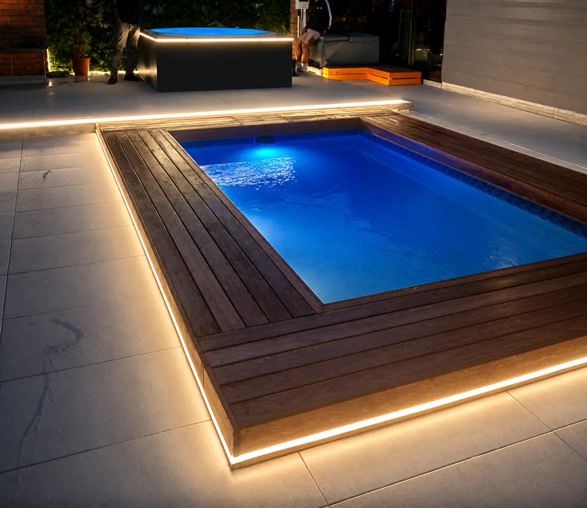 In-ground pool and raised spa lit at night with blue underwater lights and warm LED strips
