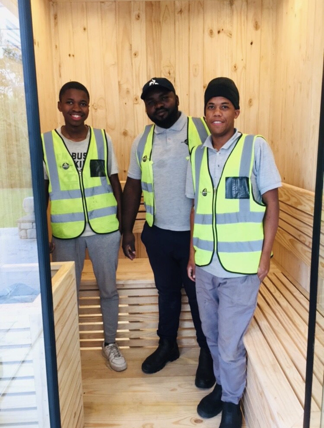 Three technicians in high-visibility vests standing inside a finished sauna cabin