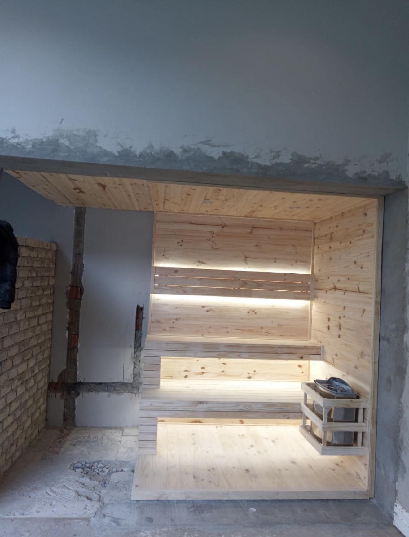 Built-in wooden sauna with warm LED strip lighting and a rock heater