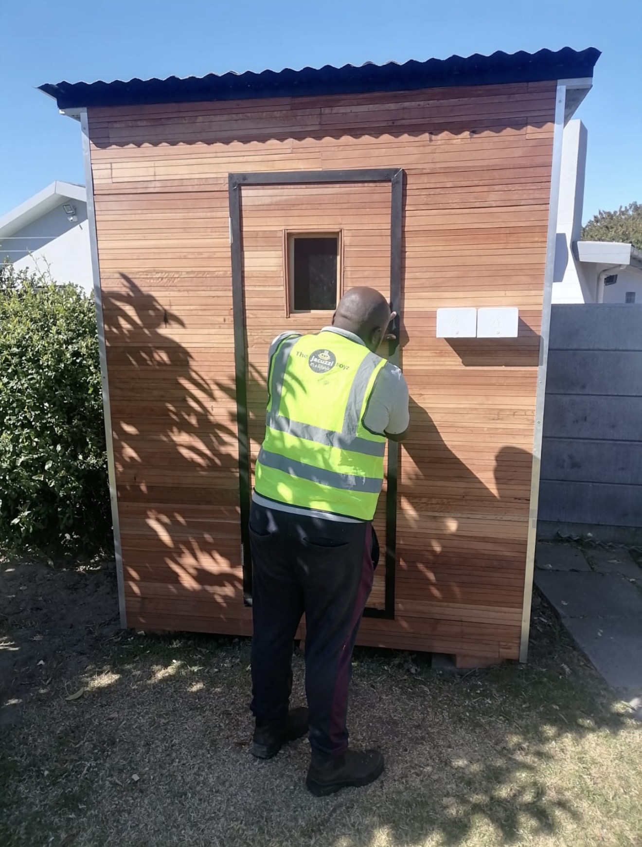 Technician fitting the black-framed door on a standalone garden sauna cabin